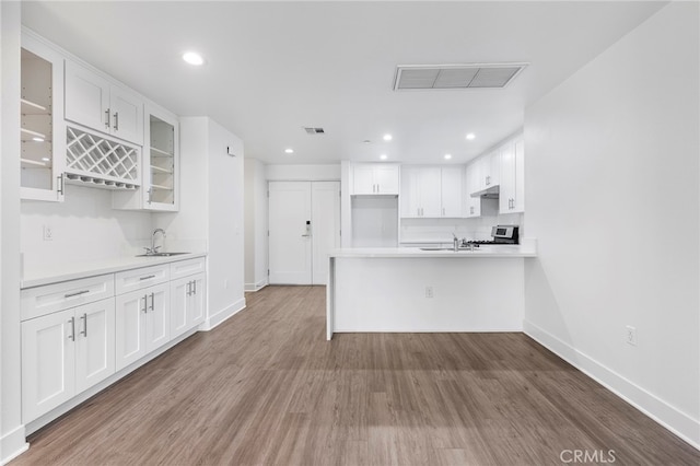 kitchen with white cabinetry, sink, stainless steel stove, and hardwood / wood-style flooring