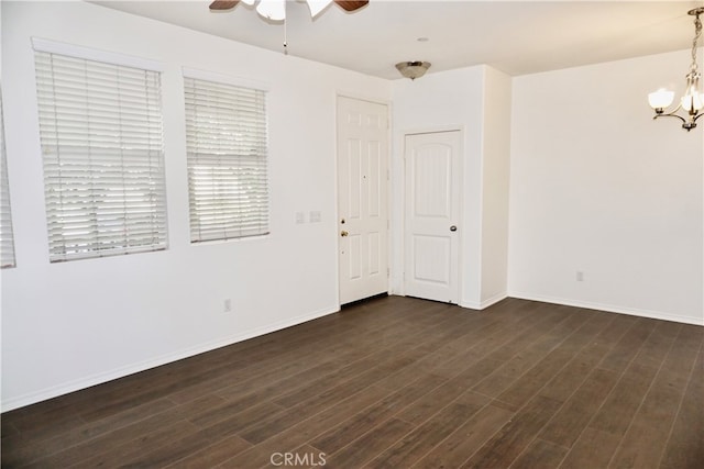 empty room featuring ceiling fan with notable chandelier and dark hardwood / wood-style flooring