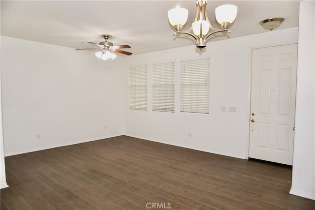 spare room with ceiling fan with notable chandelier and dark wood-type flooring