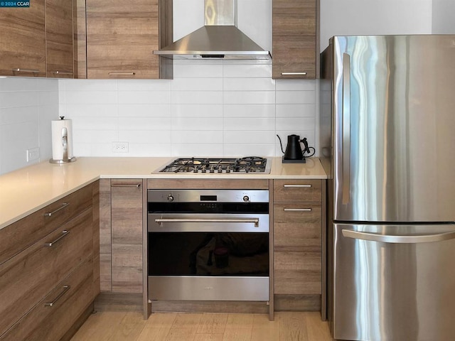 kitchen featuring backsplash, wall chimney range hood, stainless steel appliances, and light hardwood / wood-style flooring