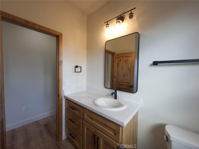 half bathroom featuring toilet, vanity, baseboards, and wood finished floors