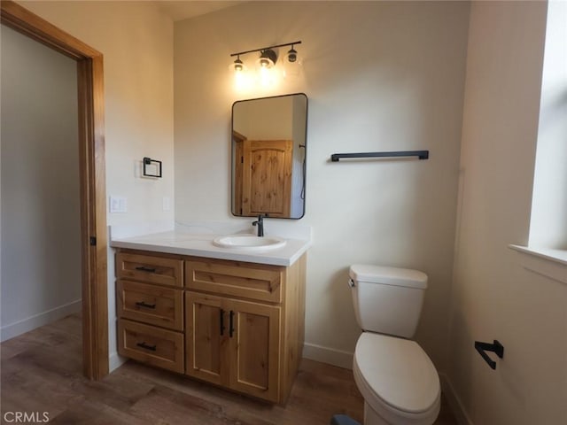 half bathroom featuring baseboards, toilet, wood finished floors, and vanity