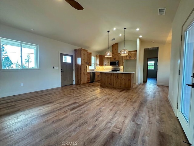 kitchen with brown cabinets, wood finished floors, open floor plan, appliances with stainless steel finishes, and light countertops