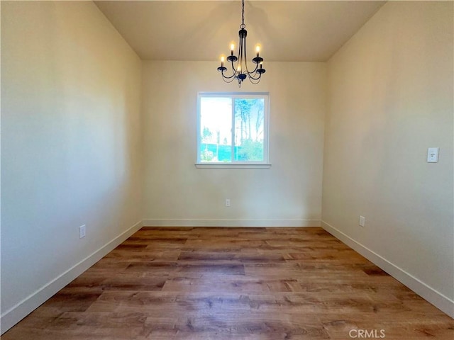 empty room featuring wood finished floors, baseboards, and a chandelier