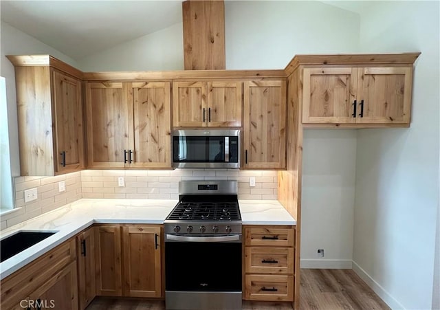 kitchen featuring tasteful backsplash, baseboards, light wood-type flooring, lofted ceiling, and appliances with stainless steel finishes