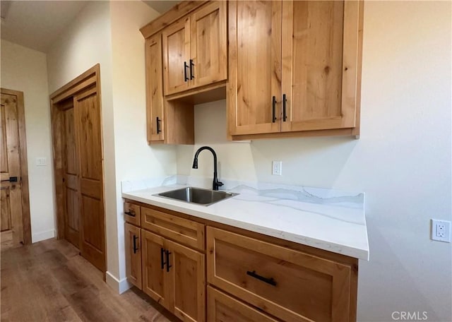 kitchen featuring wood finished floors, baseboards, light stone countertops, and a sink