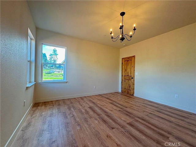 empty room with baseboards, wood finished floors, and a chandelier