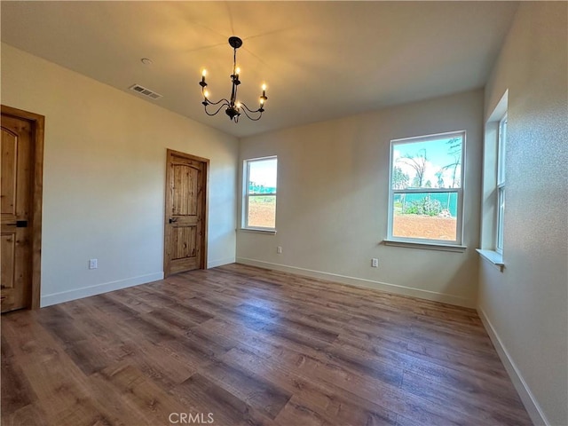 unfurnished room with a chandelier, visible vents, dark wood finished floors, and baseboards