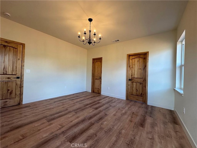 empty room featuring visible vents, baseboards, a chandelier, and dark wood finished floors