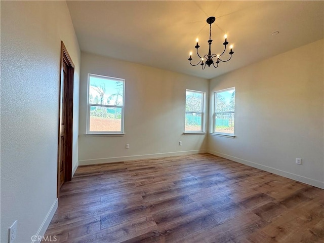 empty room featuring an inviting chandelier, wood finished floors, and baseboards