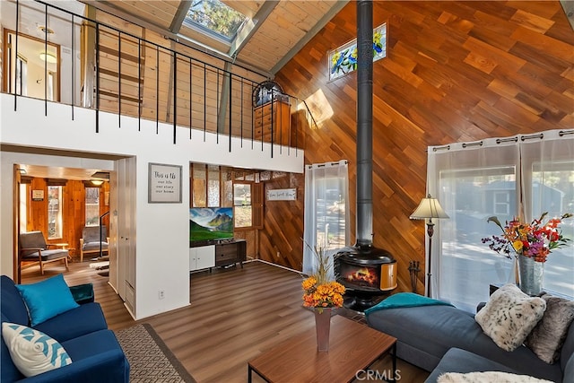 living room featuring high vaulted ceiling, a wood stove, wood walls, and a skylight