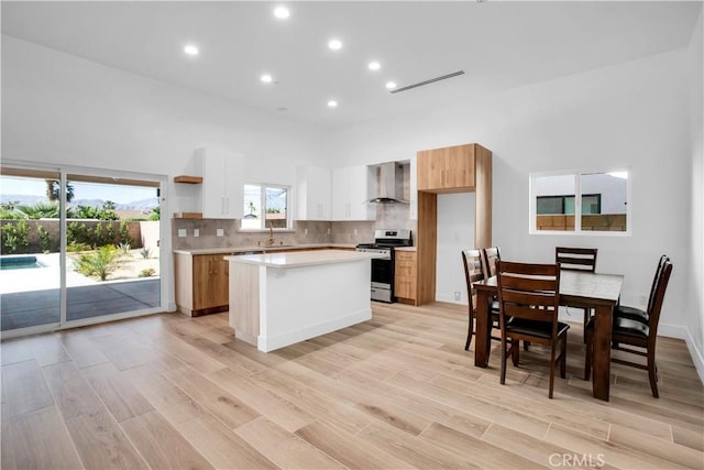 kitchen featuring white cabinetry, a center island, wall chimney exhaust hood, stainless steel range oven, and light hardwood / wood-style floors