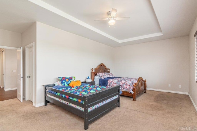 carpeted bedroom with a raised ceiling and ceiling fan