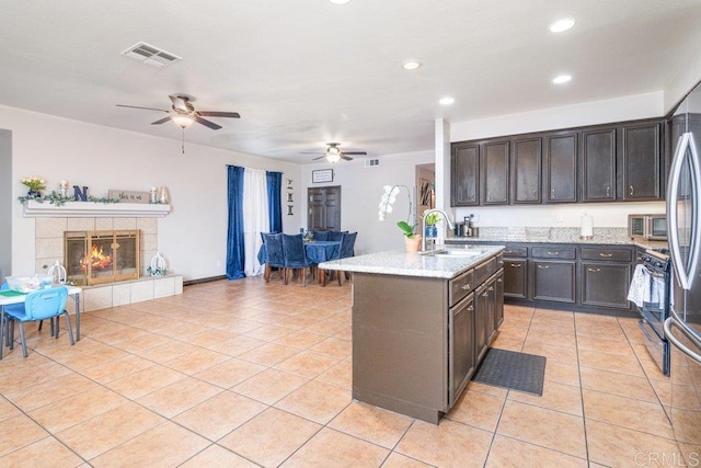 kitchen featuring dark brown cabinets, sink, light tile patterned floors, a fireplace, and an island with sink