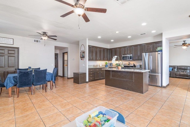 kitchen featuring light tile patterned floors, stainless steel appliances, dark brown cabinets, and a center island with sink