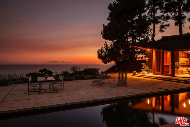 pool at dusk featuring a patio and a water view