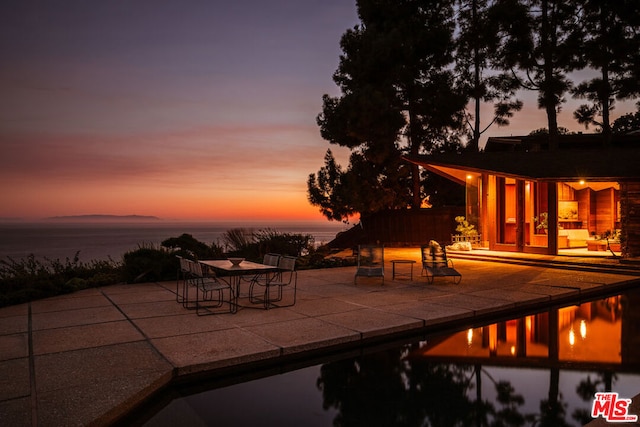 pool at dusk featuring a water view and a patio area