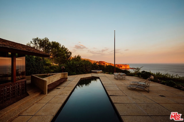 pool at dusk with a water view and a patio area