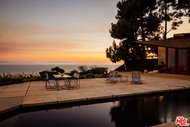 pool at dusk featuring a water view and a patio