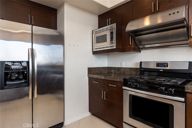 kitchen with dark stone counters, dark brown cabinets, light tile patterned flooring, stainless steel appliances, and exhaust hood