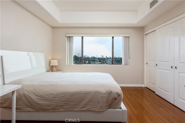 bedroom with a closet, hardwood / wood-style floors, and a tray ceiling