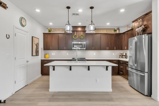 kitchen with decorative light fixtures, dark brown cabinets, stainless steel appliances, and an island with sink