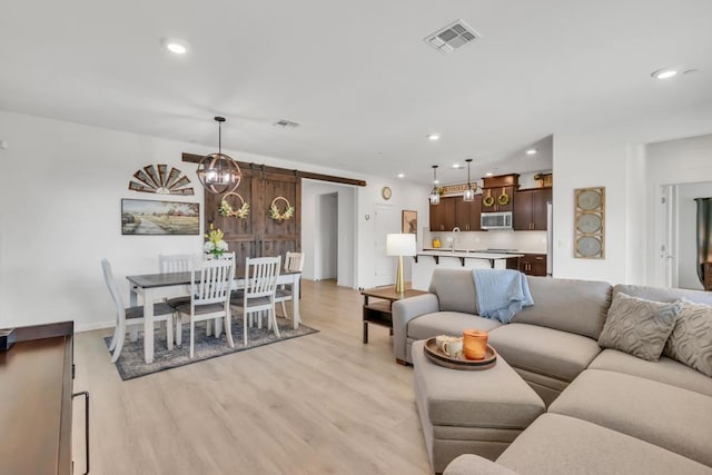 living room featuring an inviting chandelier, a barn door, light hardwood / wood-style flooring, and sink