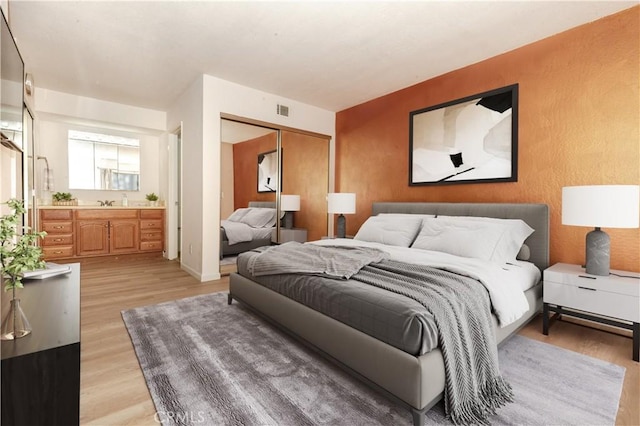 bedroom with ensuite bathroom, a closet, and light hardwood / wood-style flooring