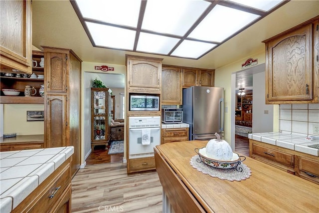 kitchen with appliances with stainless steel finishes, tile countertops, decorative backsplash, and light wood-type flooring