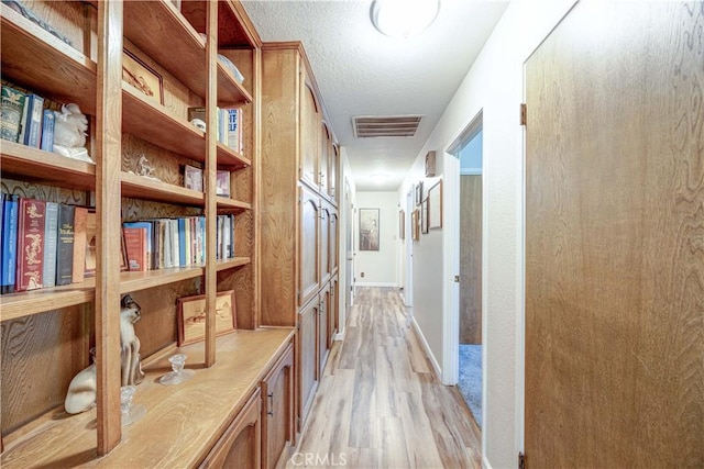 hall with a textured ceiling and light wood-type flooring