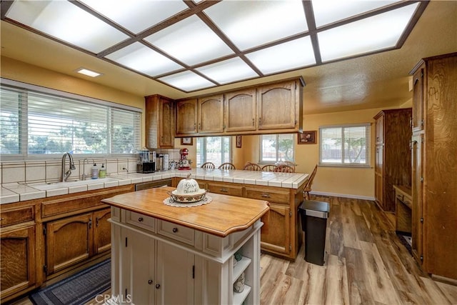 kitchen featuring a kitchen island, a wealth of natural light, tile countertops, sink, and light wood-type flooring