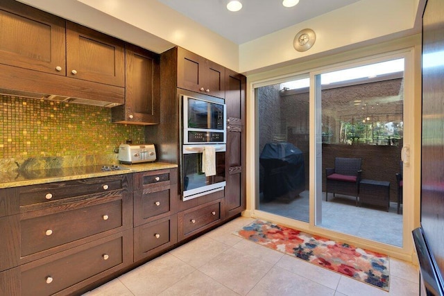 kitchen with stainless steel microwave, light tile patterned floors, backsplash, and stovetop