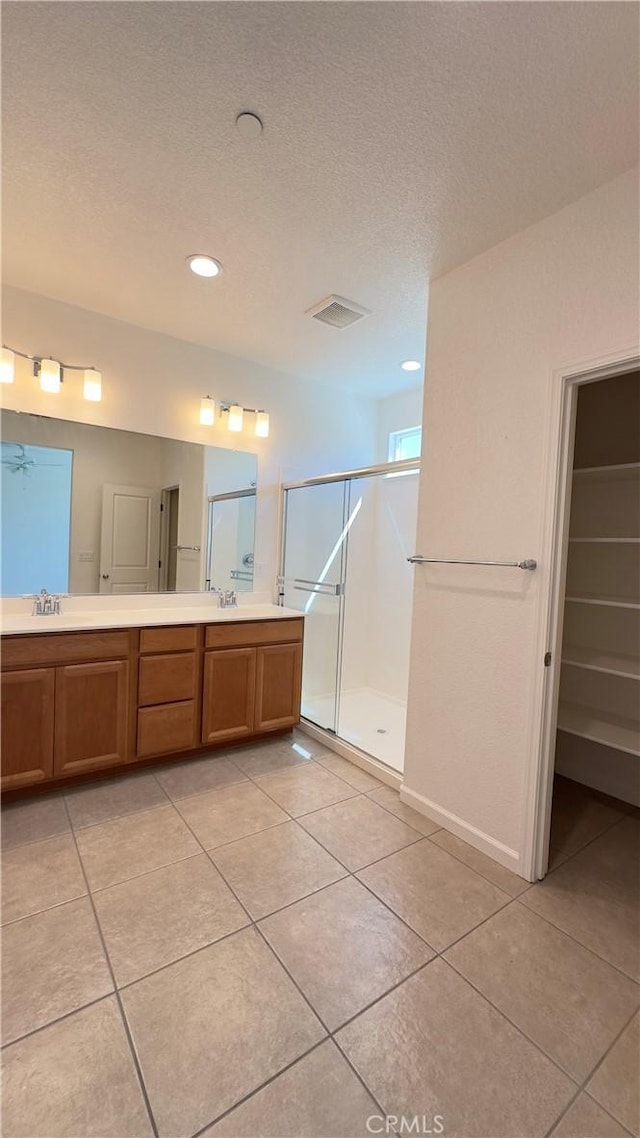 bathroom with a shower with shower door, tile patterned flooring, vanity, ceiling fan, and a textured ceiling