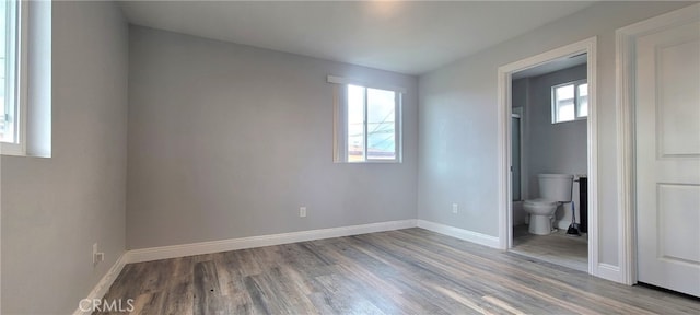 unfurnished bedroom with light wood-type flooring, connected bathroom, and multiple windows