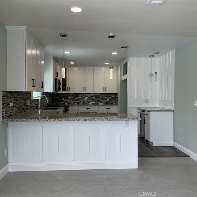 kitchen featuring kitchen peninsula, light stone counters, and pendant lighting