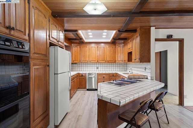 kitchen featuring white refrigerator, double oven, tile counters, light hardwood / wood-style floors, and decorative backsplash