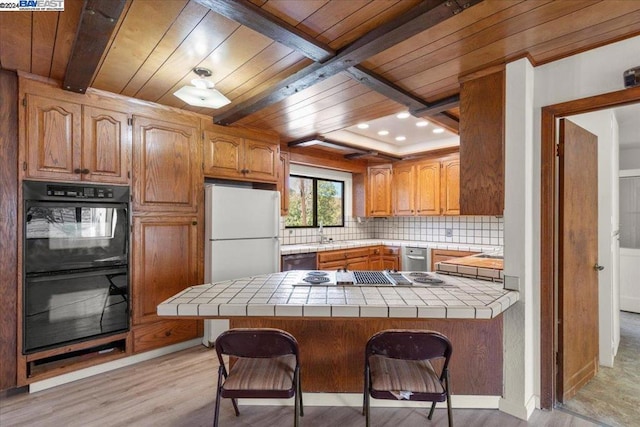 kitchen with a kitchen breakfast bar, kitchen peninsula, stainless steel appliances, and tile countertops