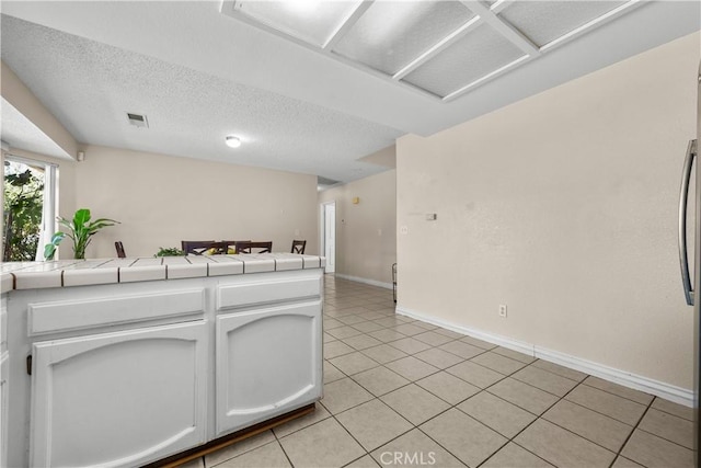 kitchen with light tile patterned floors, tile countertops, kitchen peninsula, a textured ceiling, and white cabinets