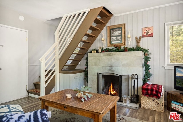 living room featuring crown molding, wood walls, a tiled fireplace, and dark hardwood / wood-style flooring