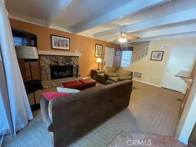 living room featuring beam ceiling, ceiling fan, a fireplace, and light colored carpet