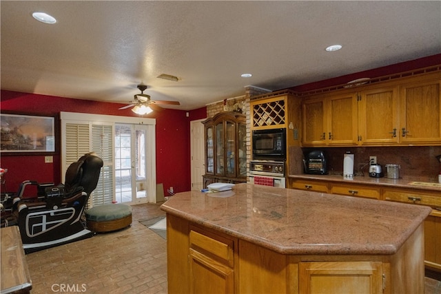 kitchen with ceiling fan, backsplash, stainless steel oven, a center island, and black microwave