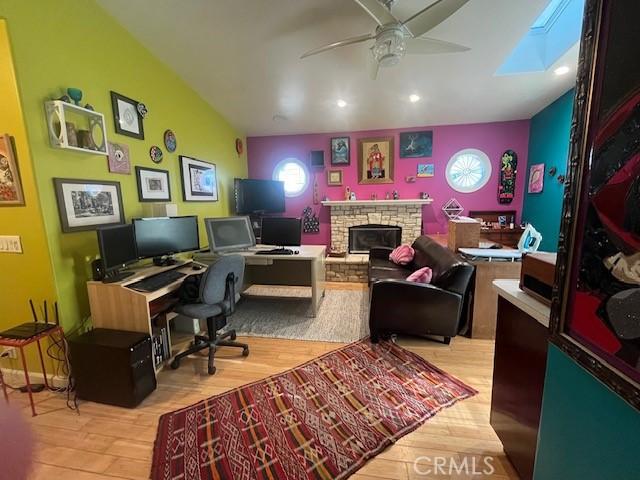 office space with lofted ceiling with skylight, ceiling fan, light wood-type flooring, and a stone fireplace