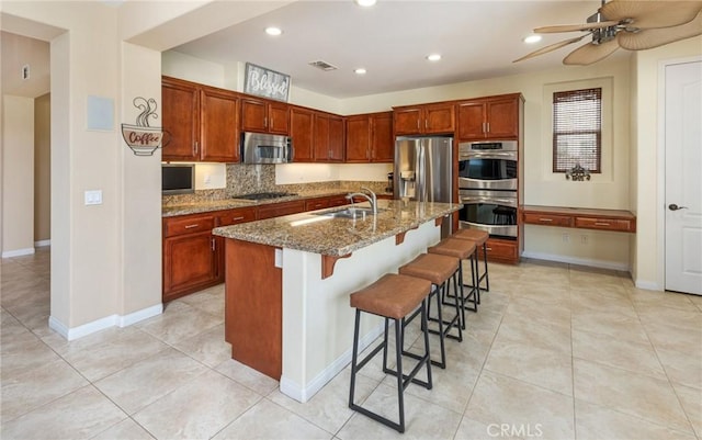 kitchen with a breakfast bar, a center island with sink, sink, ceiling fan, and appliances with stainless steel finishes