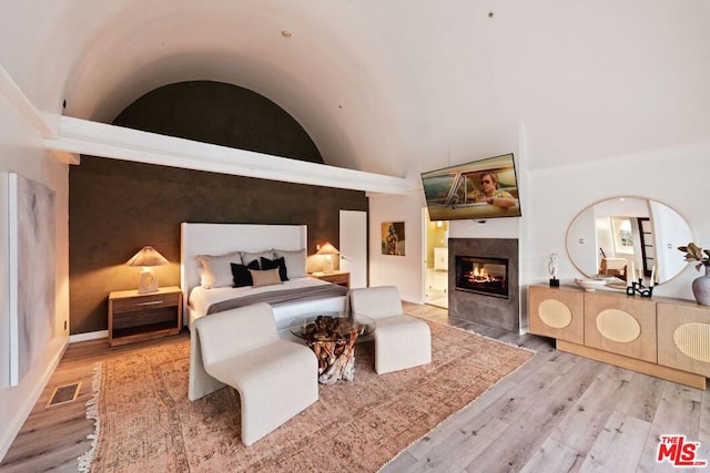 bedroom with a tiled fireplace, light hardwood / wood-style flooring, and high vaulted ceiling