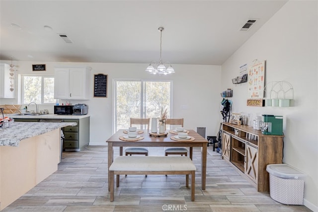 dining room with light hardwood / wood-style floors, vaulted ceiling, sink, and a chandelier