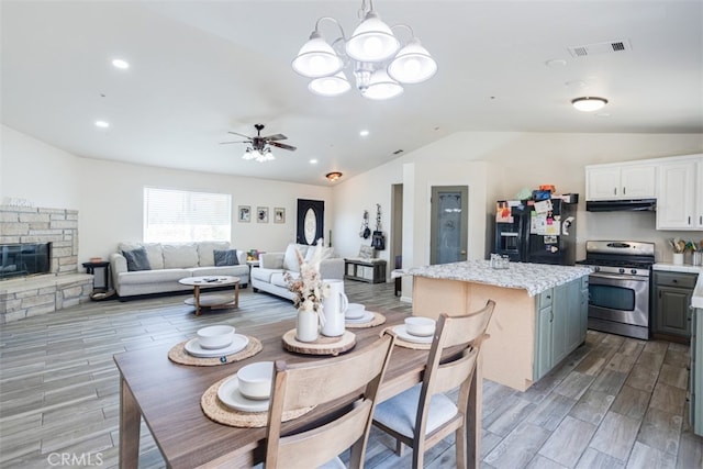 dining space featuring light wood-type flooring, ceiling fan with notable chandelier, a fireplace, and vaulted ceiling