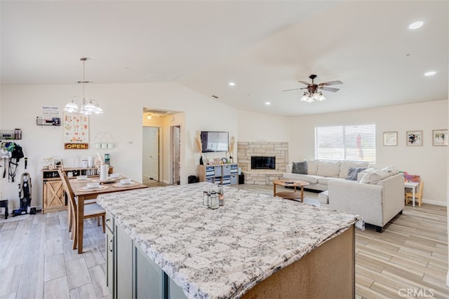 kitchen with a stone fireplace, ceiling fan with notable chandelier, light wood-type flooring, and vaulted ceiling