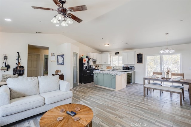 living room with ceiling fan with notable chandelier, lofted ceiling, light hardwood / wood-style floors, and sink