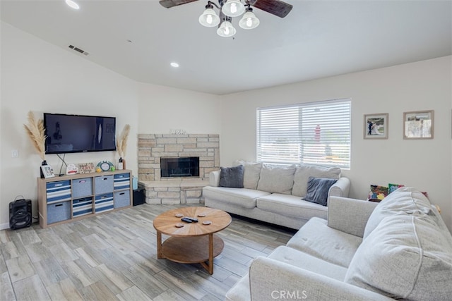 living room featuring light wood-type flooring, vaulted ceiling, ceiling fan, and a stone fireplace