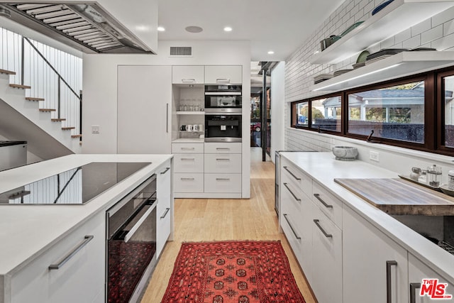 kitchen with white cabinets, light hardwood / wood-style flooring, black electric cooktop, range hood, and tasteful backsplash